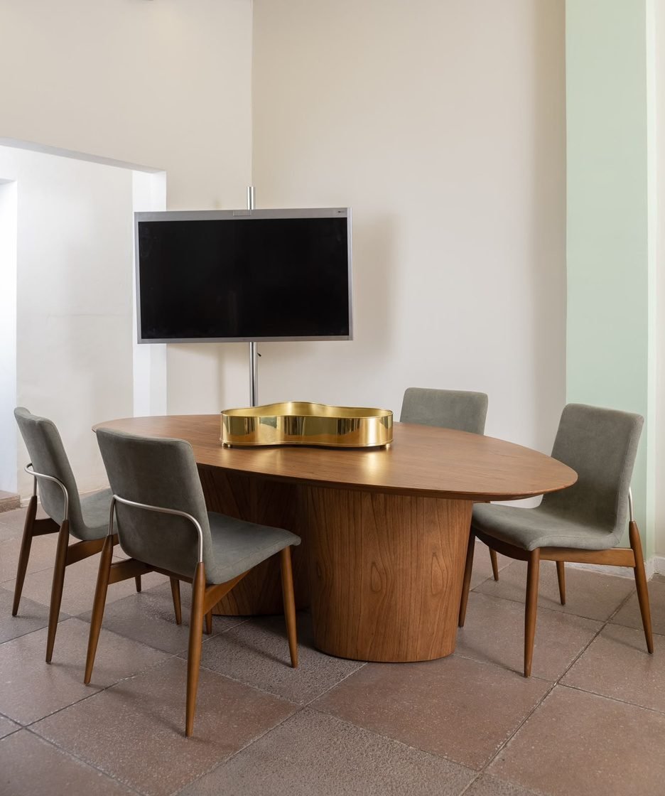 Sala de reunião com mesa oval de madeira e cadeiras estofadas